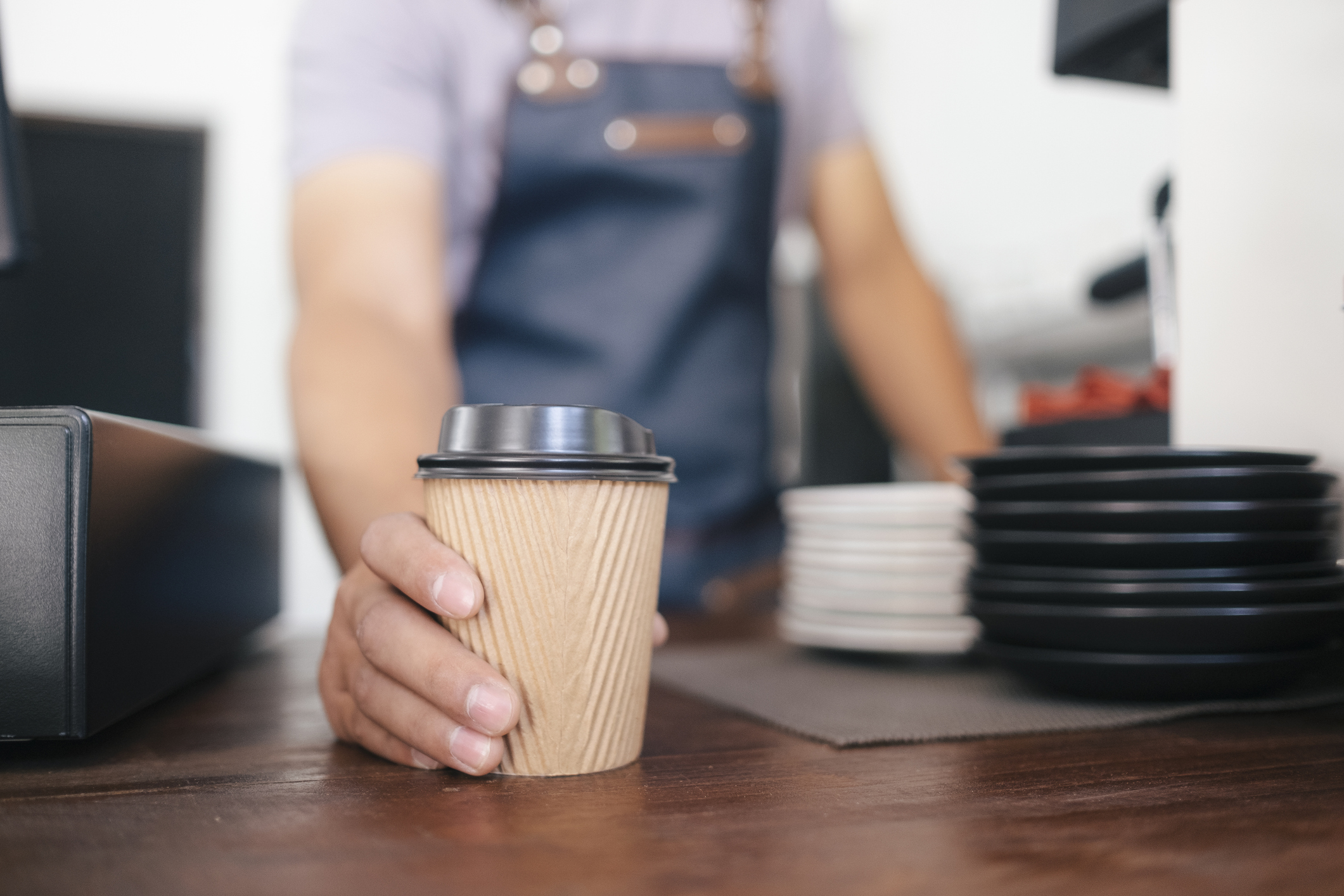 Stock Image of a Barista Sliding a Paper Cup of Coffee Toward the Camera