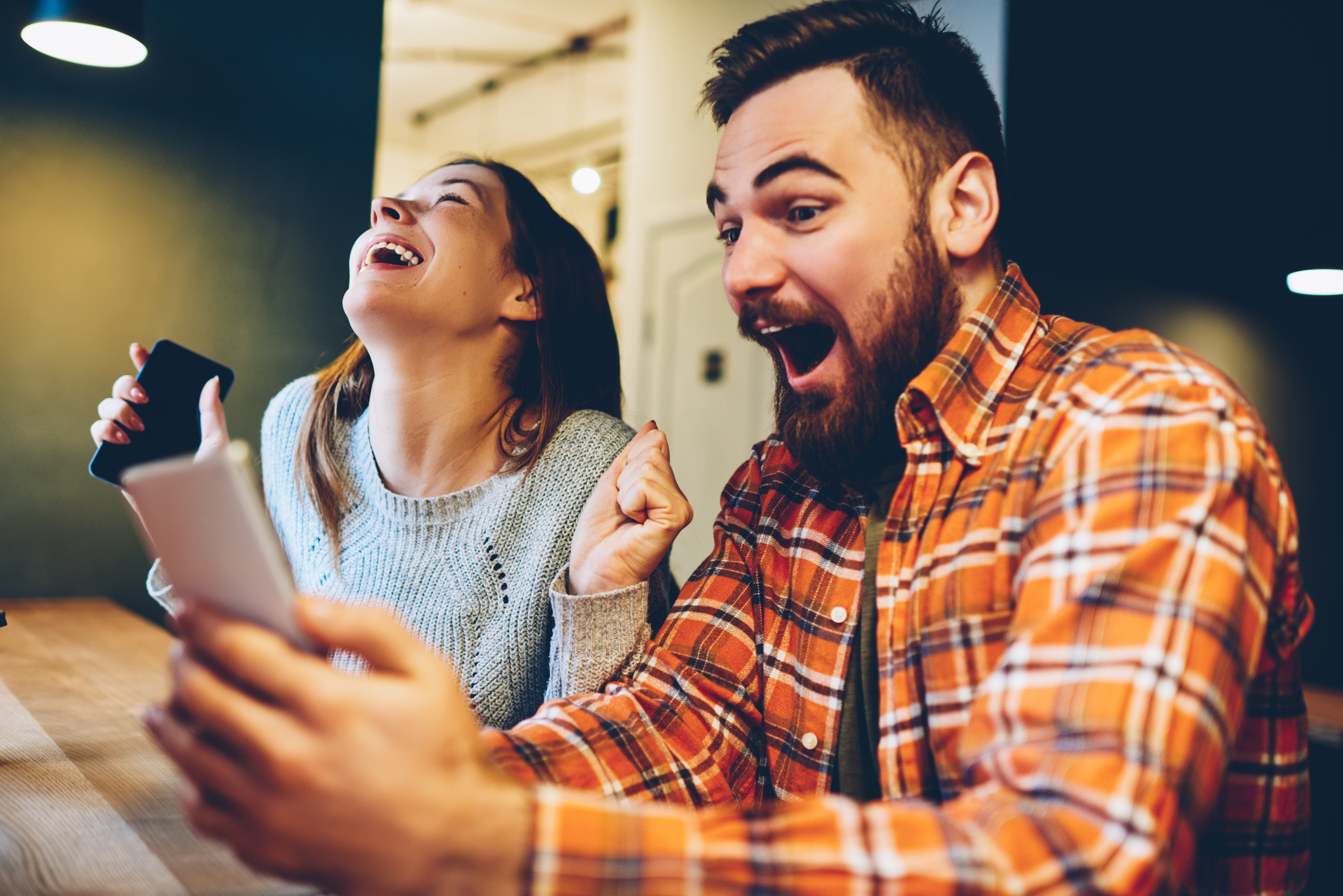 Stock Image of a Man and Woman Sitting Together And Laughing While Looking At Their Cell Phone Screens
