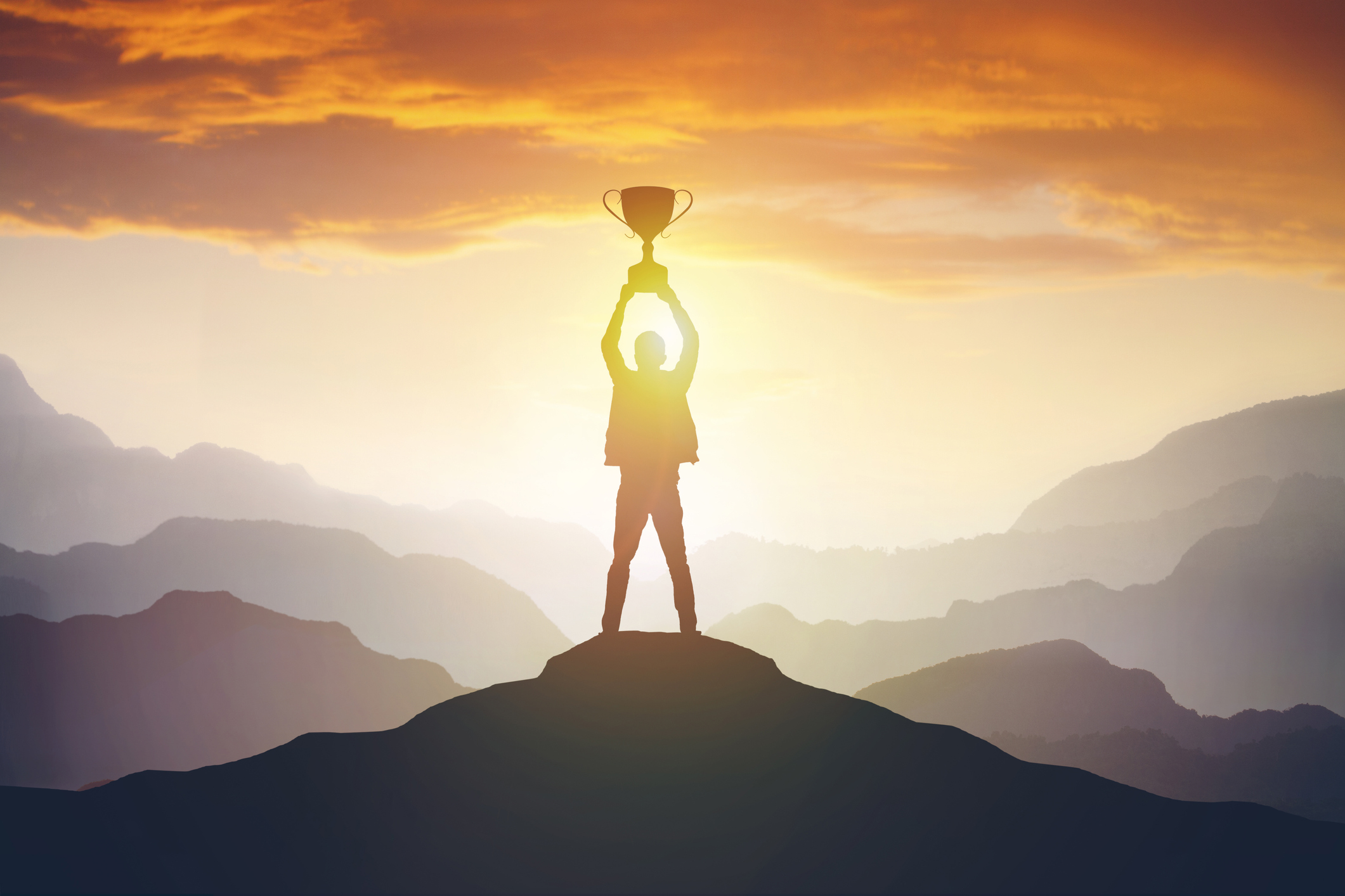 Stock Image of a Silhouette Of A Man Standing on A Mountain and Holding A Trophy Above His Head