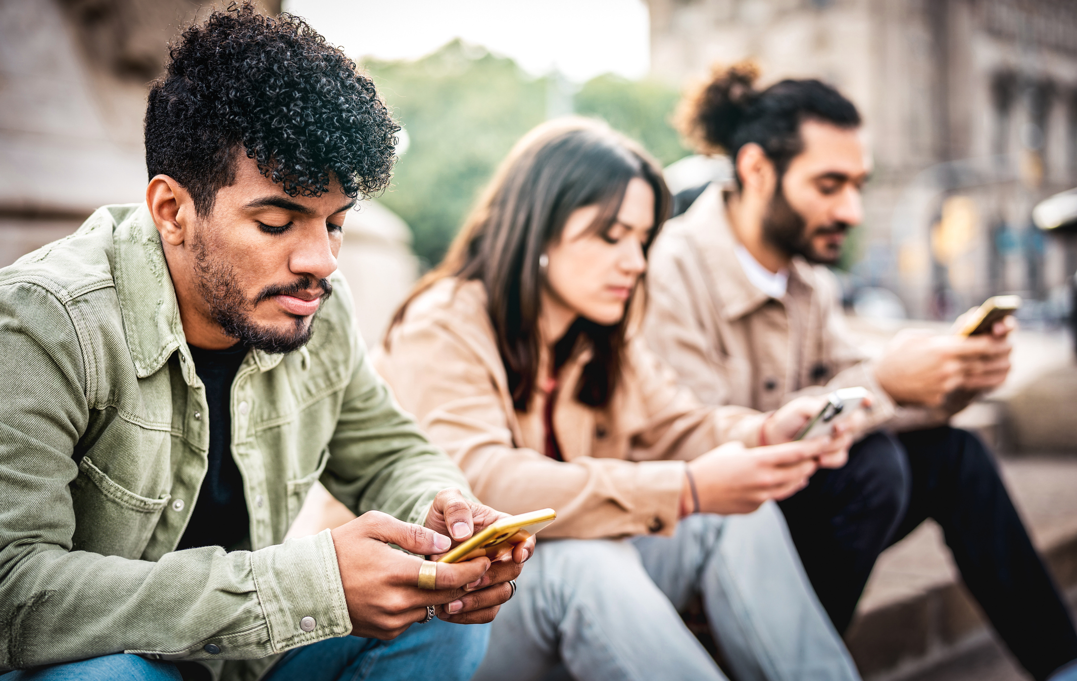 Stock Image of Three People Man Woman Man Sitting Next To One Another and All Looking at Their Phones