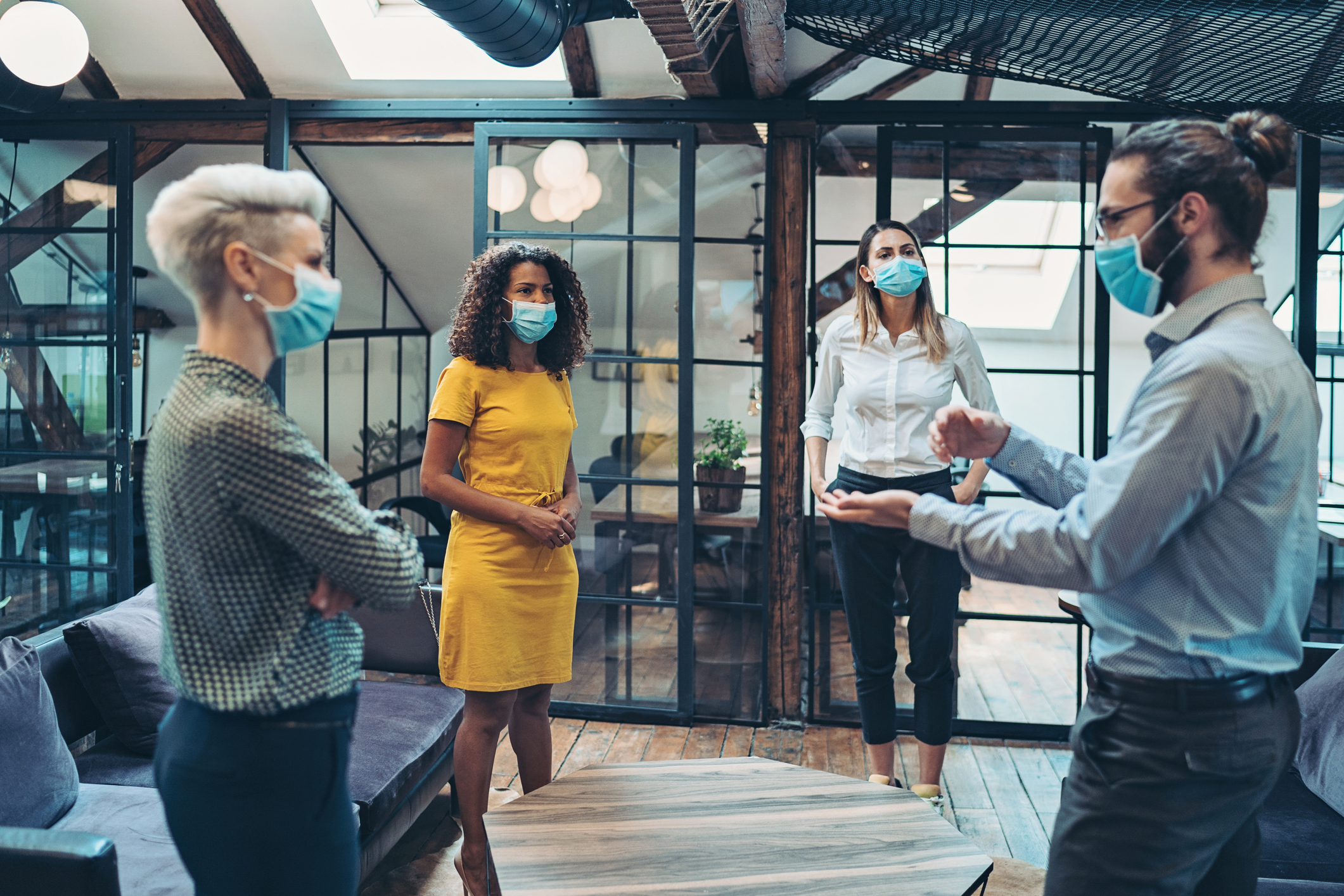 Stock Photo of Four Employees Standing in a Circle in a Meeting and Wearing Masks