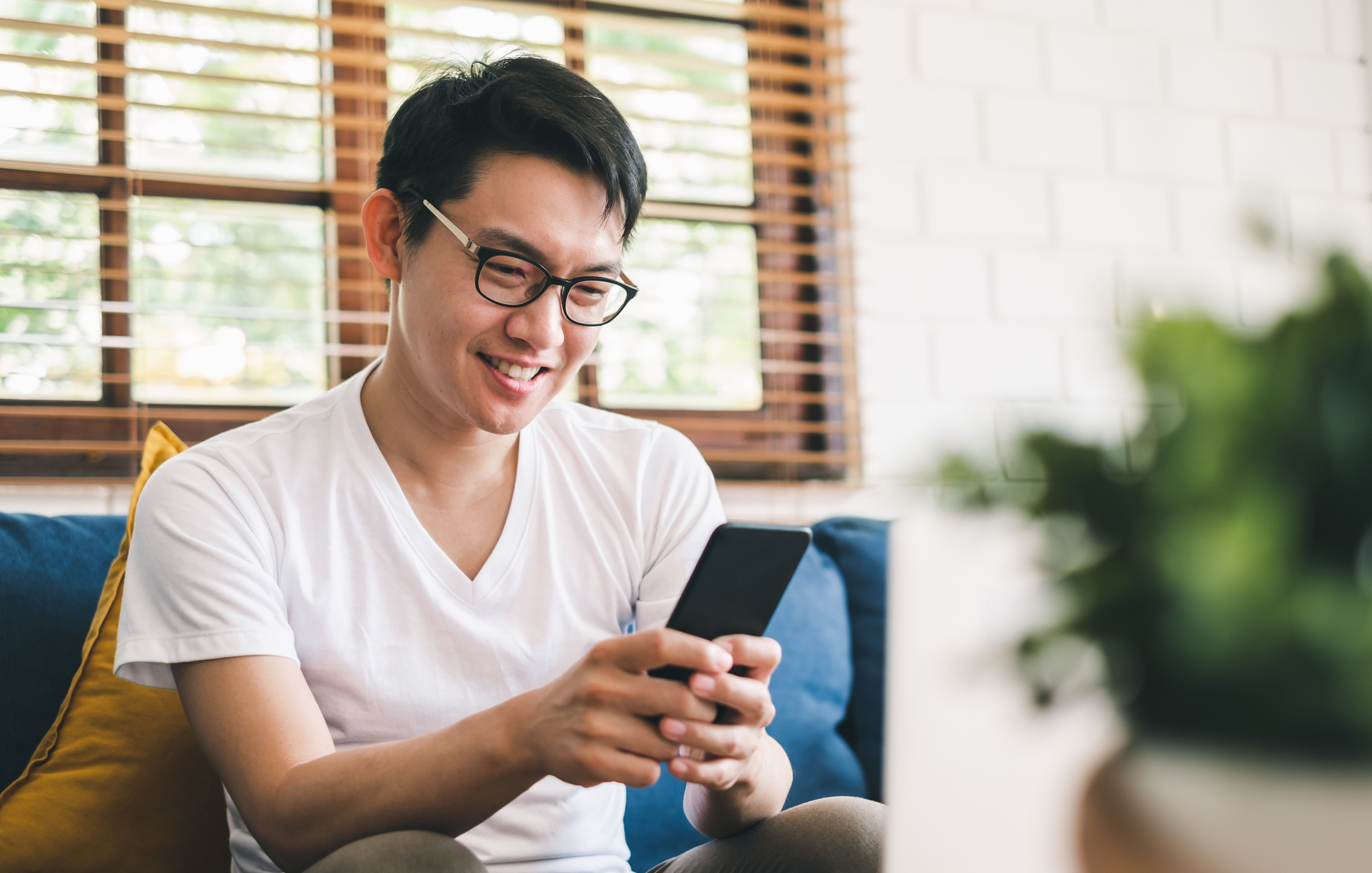 Stock Photo of Man Sitting on Sofa Looking at His Cell Phone and Smiling
