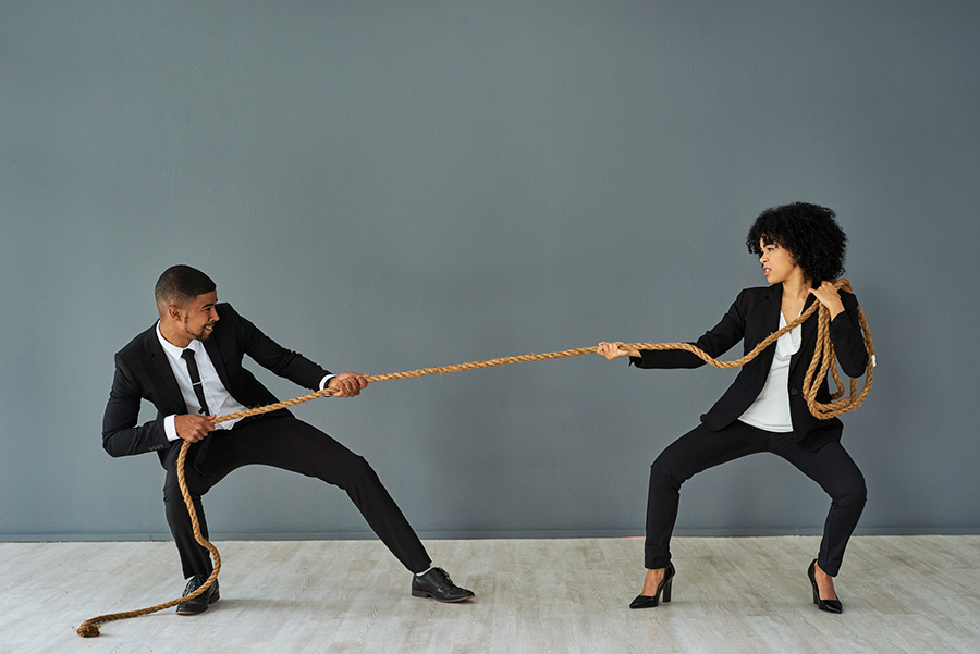 Image of a business man and woman in suits, each pulling at opposite ends of a rope. 