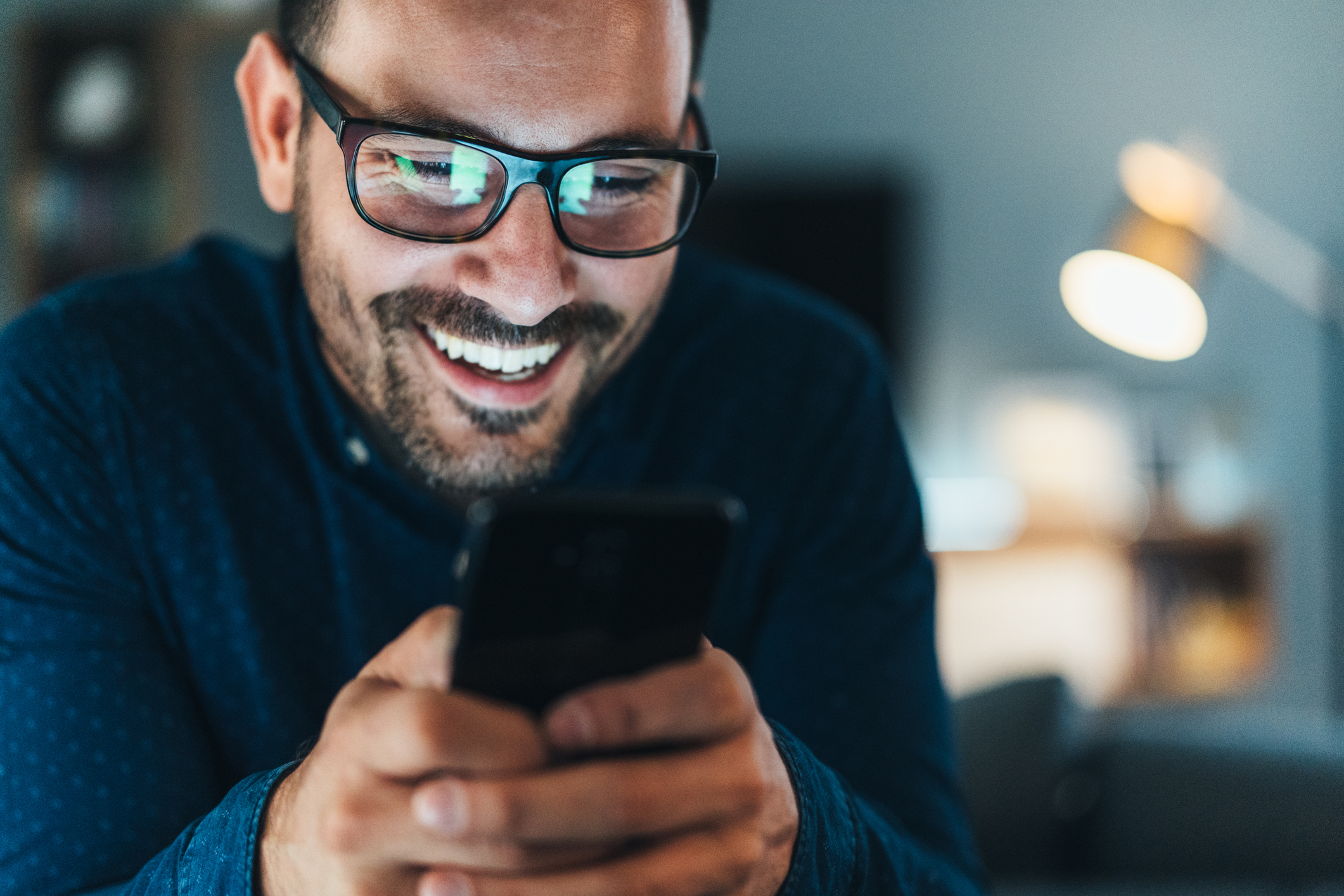 Stock image of a man holding a cell phone and typing a message while smiling. 