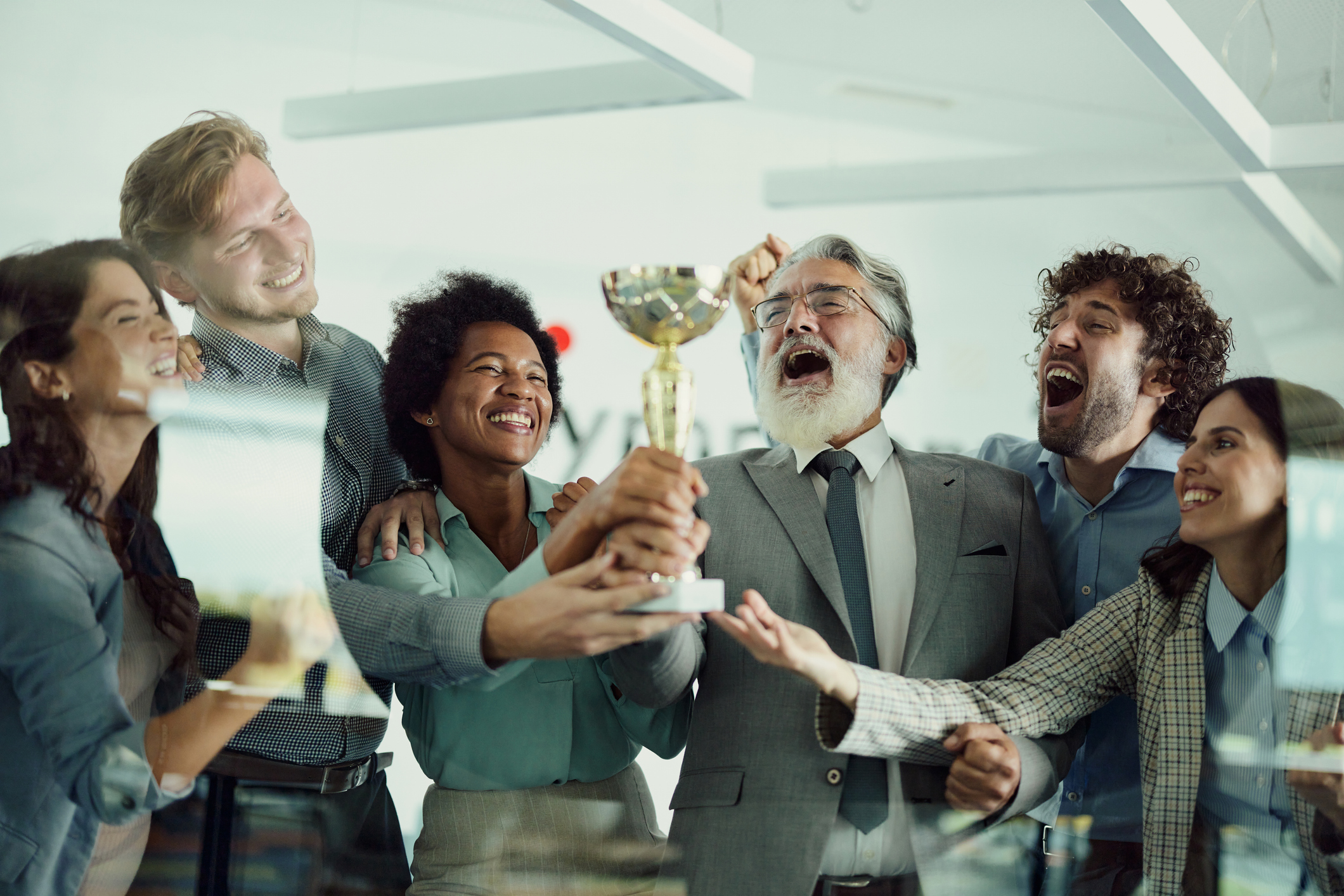 Stock image of a multicultural and multigenerational team holding up a trophy and celebrating. 