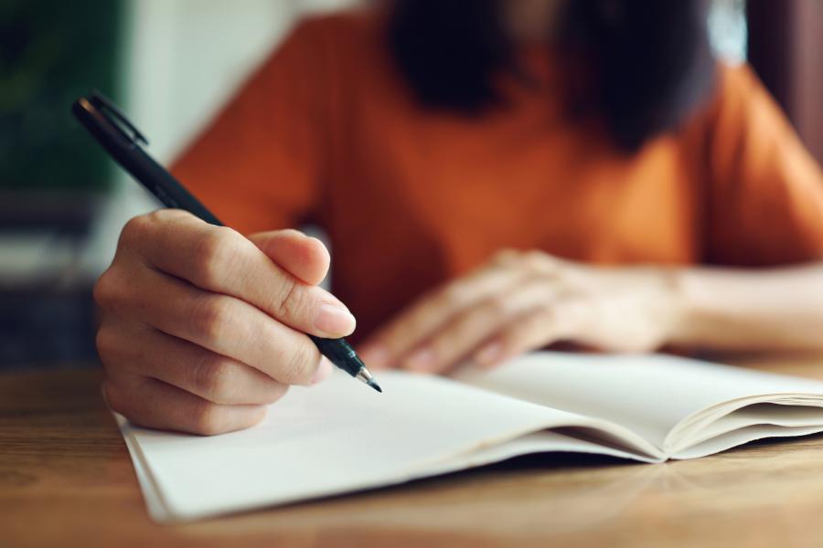 Stock image of a woman's hand holding a pen and writing in a journal.