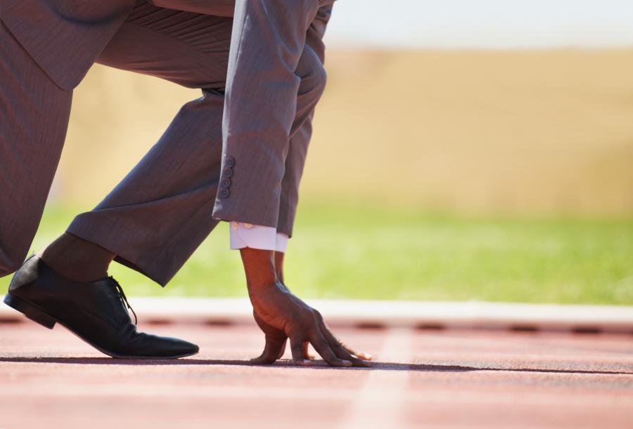 Stock image of a man in a business suit crouched down on the starting line of a track.