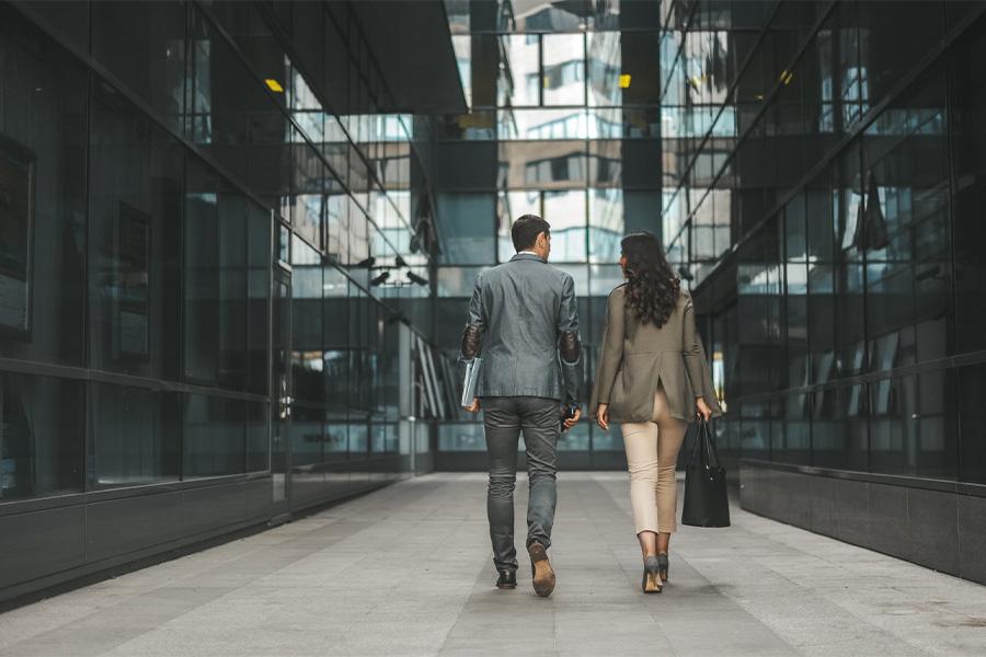view from behind a business man and woman walking into an urban glass front building