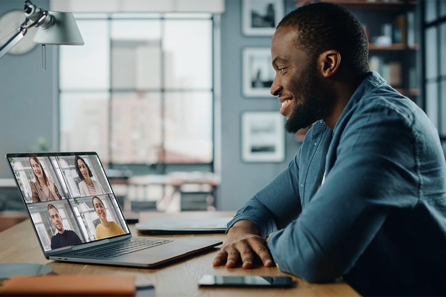 Business man sitting in office looking at laptop and smiling at colleagues who appear on the laptop screen on a virtual call