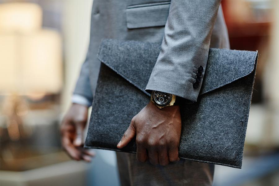 close up image of a man's arm holding a designer bag with an expensive watch peeking out under his suit sleeve