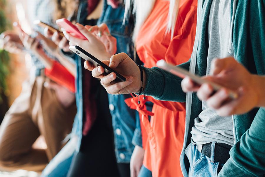 close up image of the hands of six people standing in a line all holding their cell phones and looking down at their cell phones