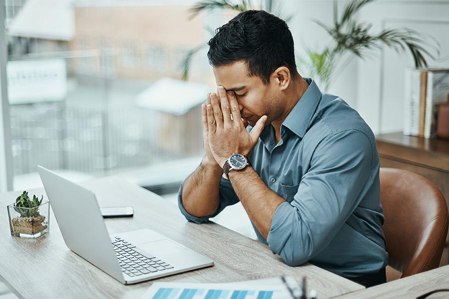 stock image of a man sitting at a desk in front of a laptop with his face in his hands