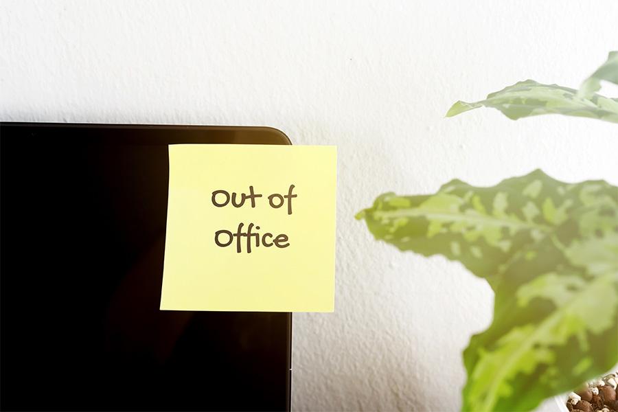 close up image of a yellow sticky note with the words "out of office" is stuck on a  computer monitor that is turned off