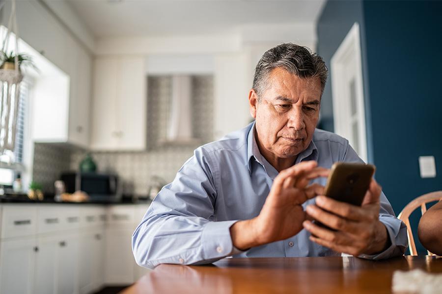 older hispanic man sitting at kitchen table looking at cell phone