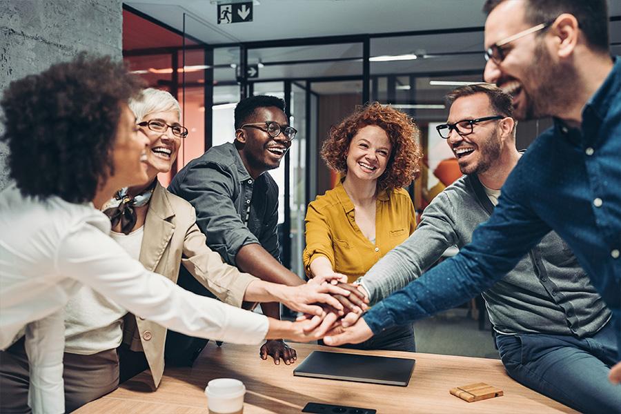 stock image of a multiracial team standing in an office and putting their hands in together to relfect teamwork
