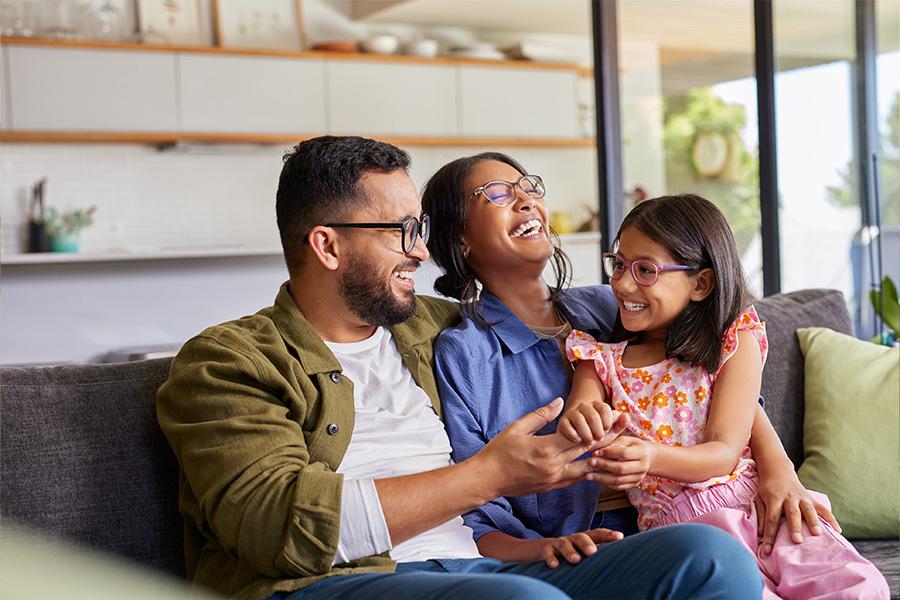 stock image of a young man and woman and their daughter sitting on the couch cuddling and laughing