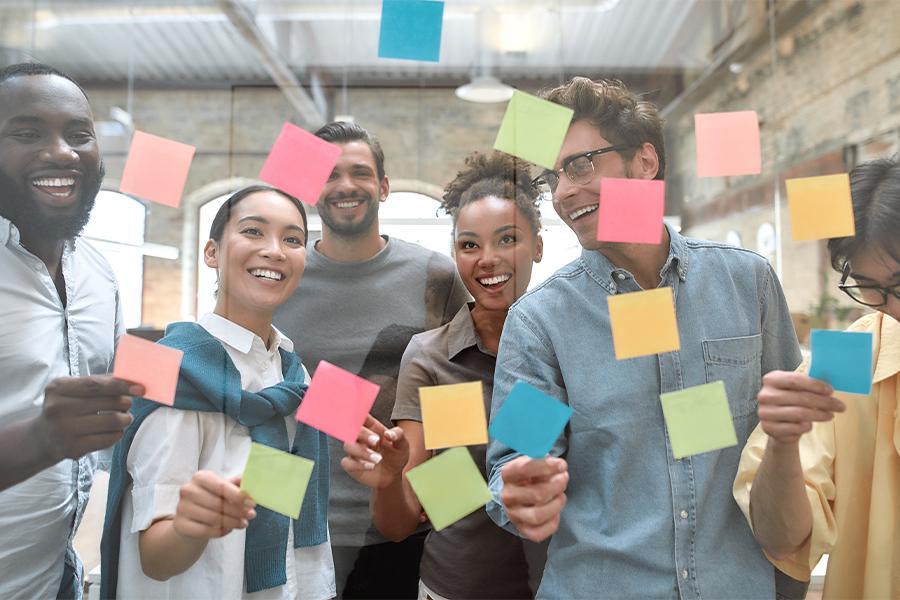 stock image looking through an office glass wall at a group of young professionals smiling and placing post-it notes on the glass