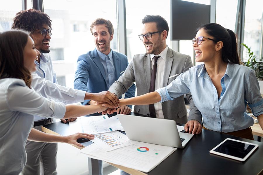 stock image of a group of young professionals standing around a stand up desk and putting their hands in a team formation