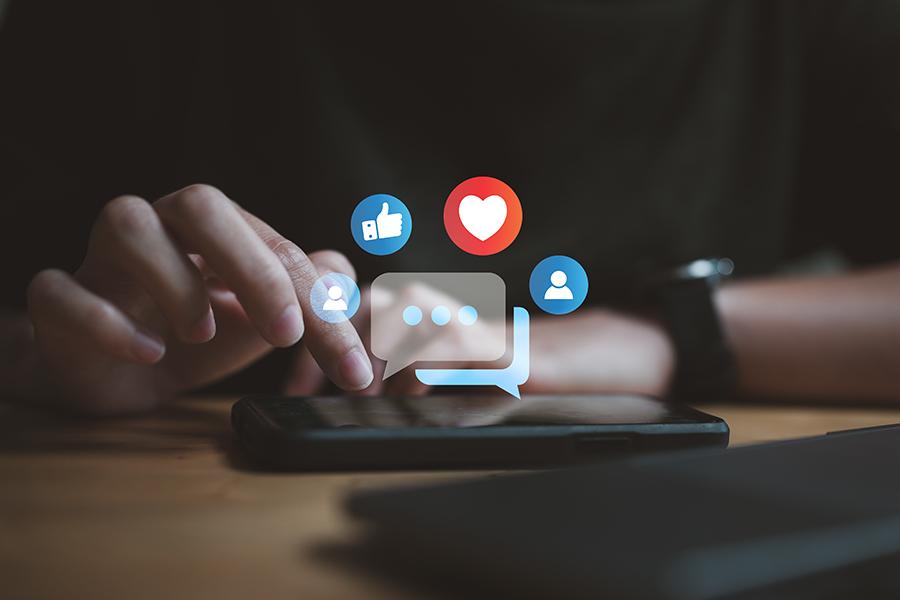 stock image, close up of woman's hands and she is scrolling a cell phone. graphic heart and thumbs up for "loves" and "likes" hover above phone